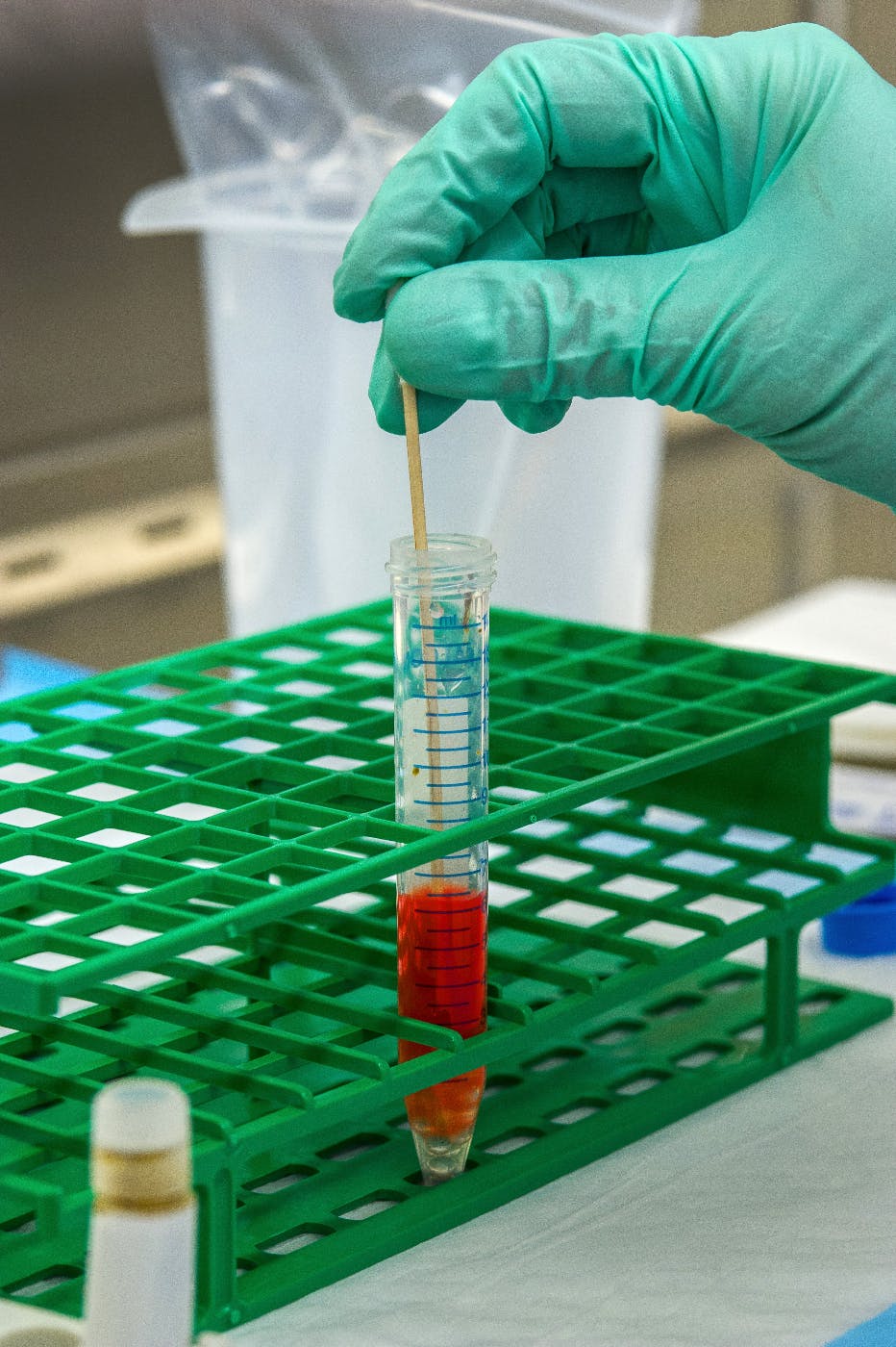 A gloved hand placing a swab into a test tube on a rack
