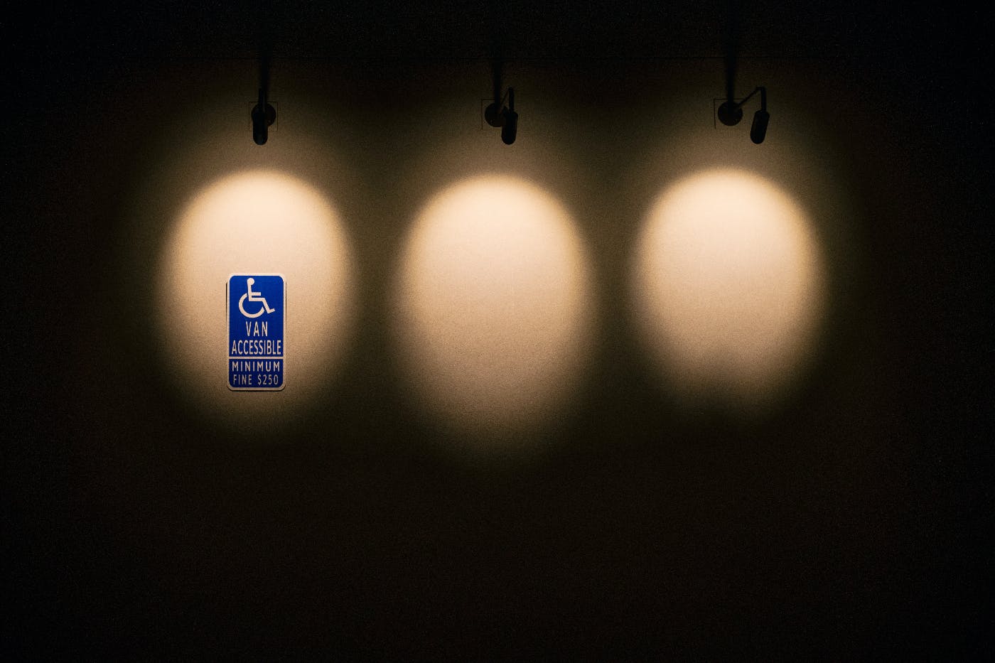 3 spot lights on a black wall, the first illuminates a handicap sign