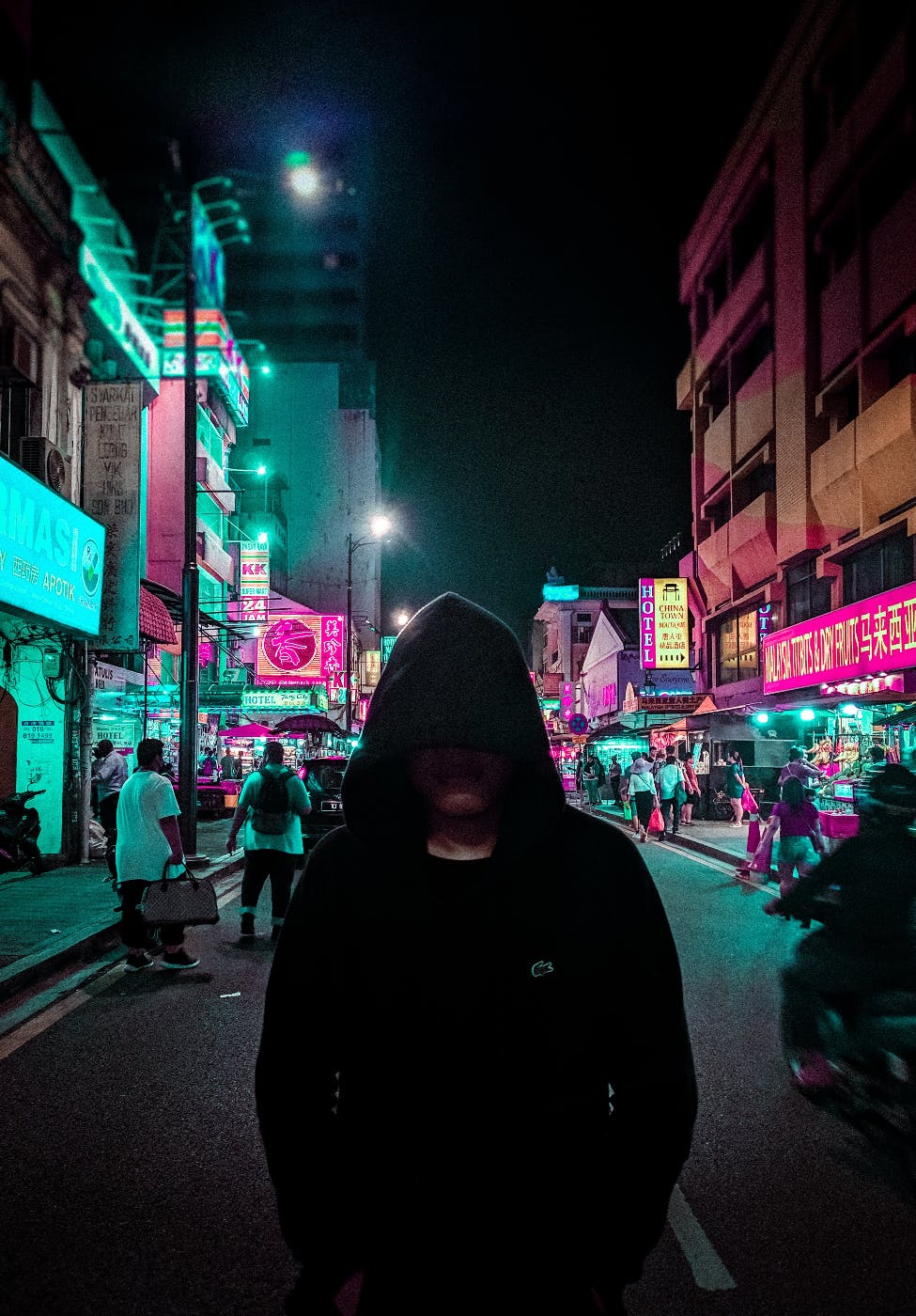 A hooded figure walking a busy street at night