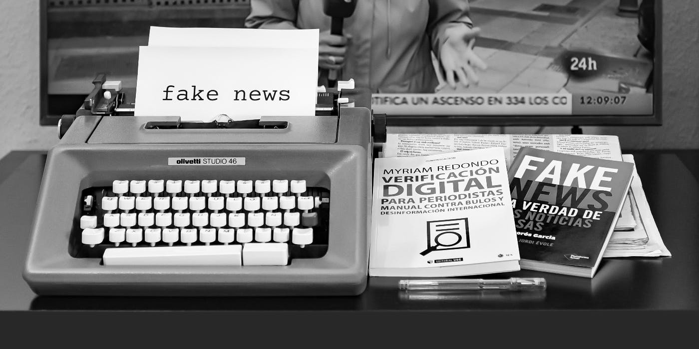 A table with an electric typewriter, magazines and a video screen all spreading fake news
