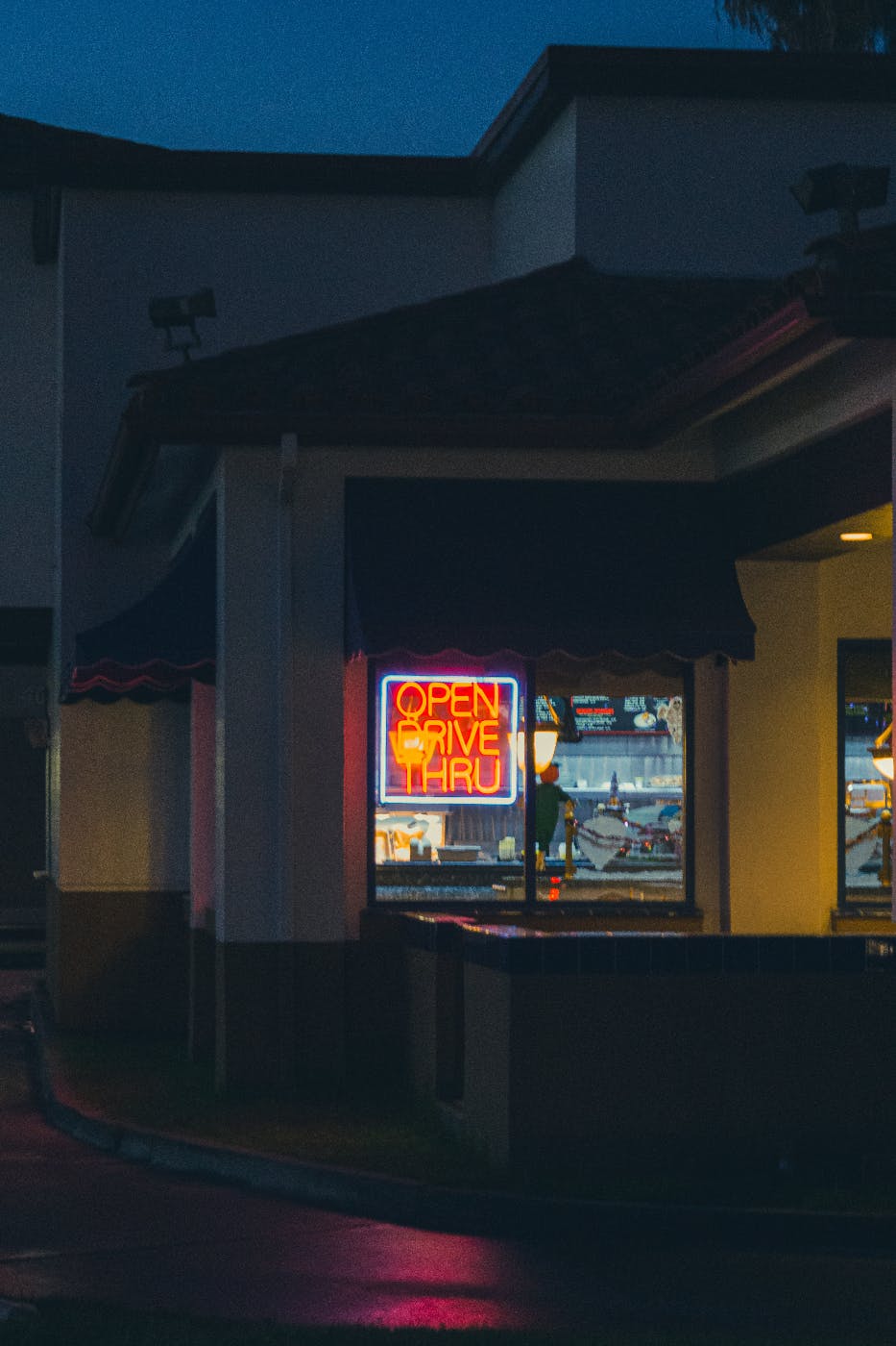A fast food restaurant with a neon sign reading drive-thu open