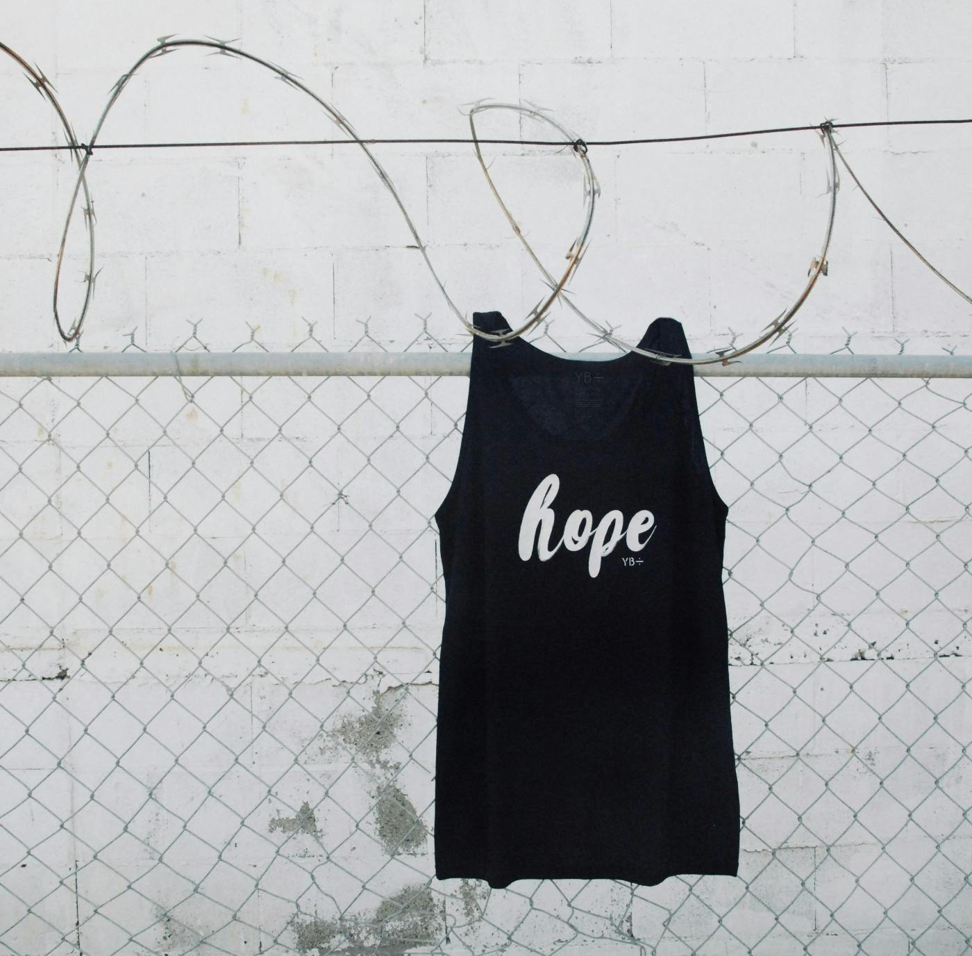 A fence with razor wire on top and a black t-shirt with the word hope hanging on the razor wire