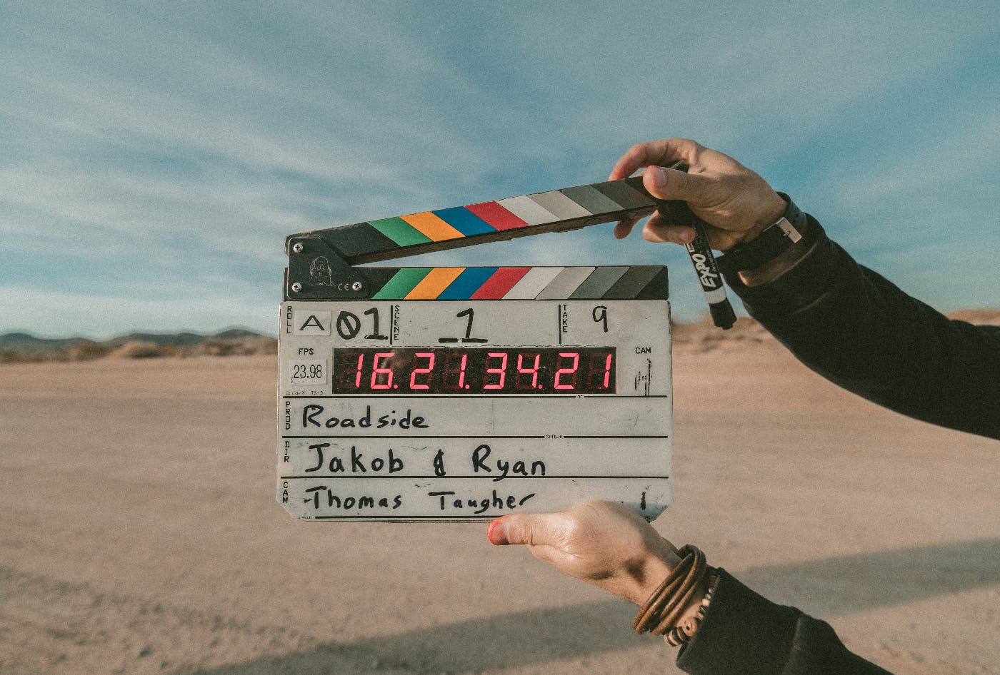 Hands holding up a film clapper in front of a desert