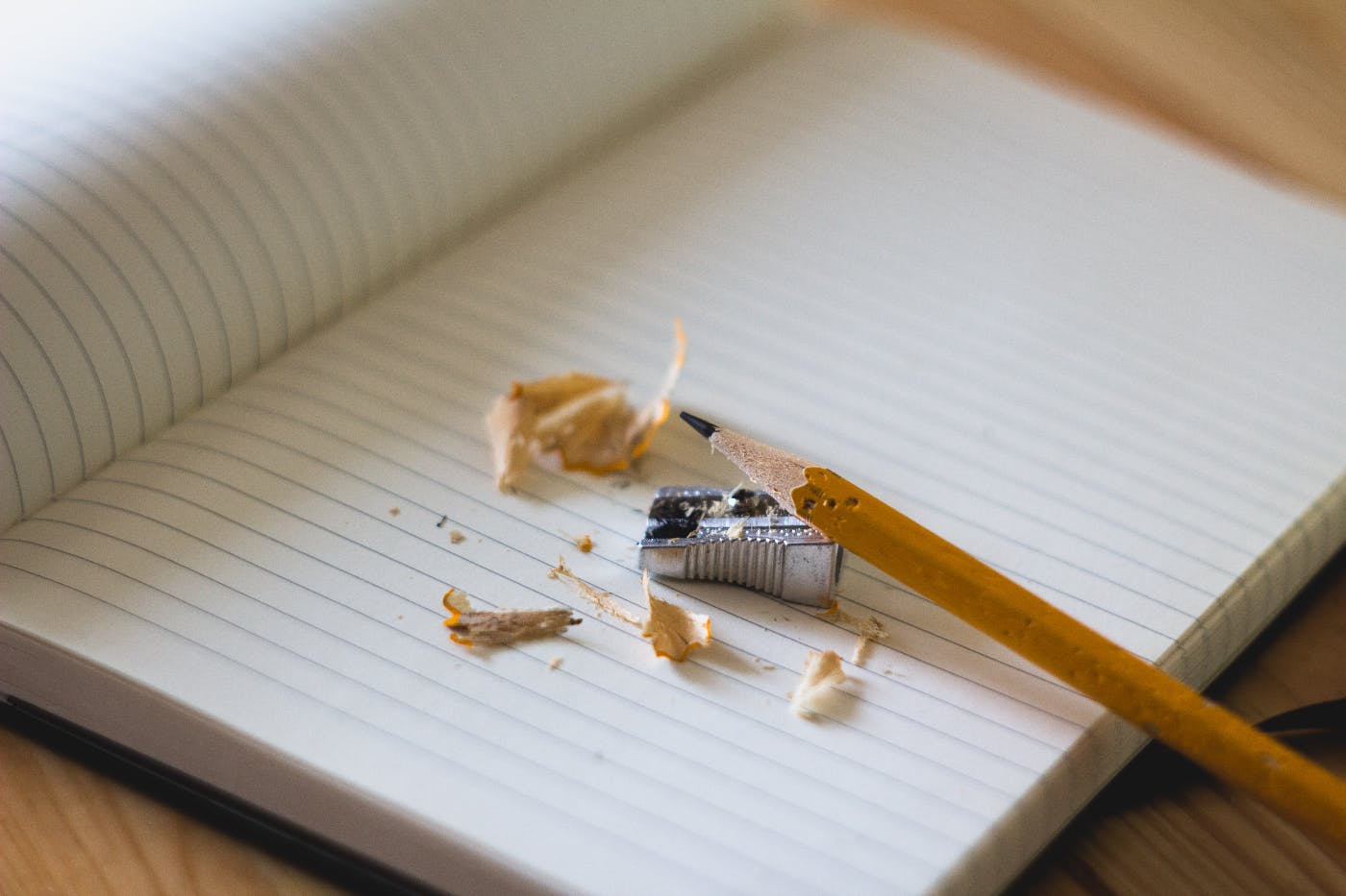 The blank page of a journal with a metal pencil sharpener, a pencil and pencil shavings on it.