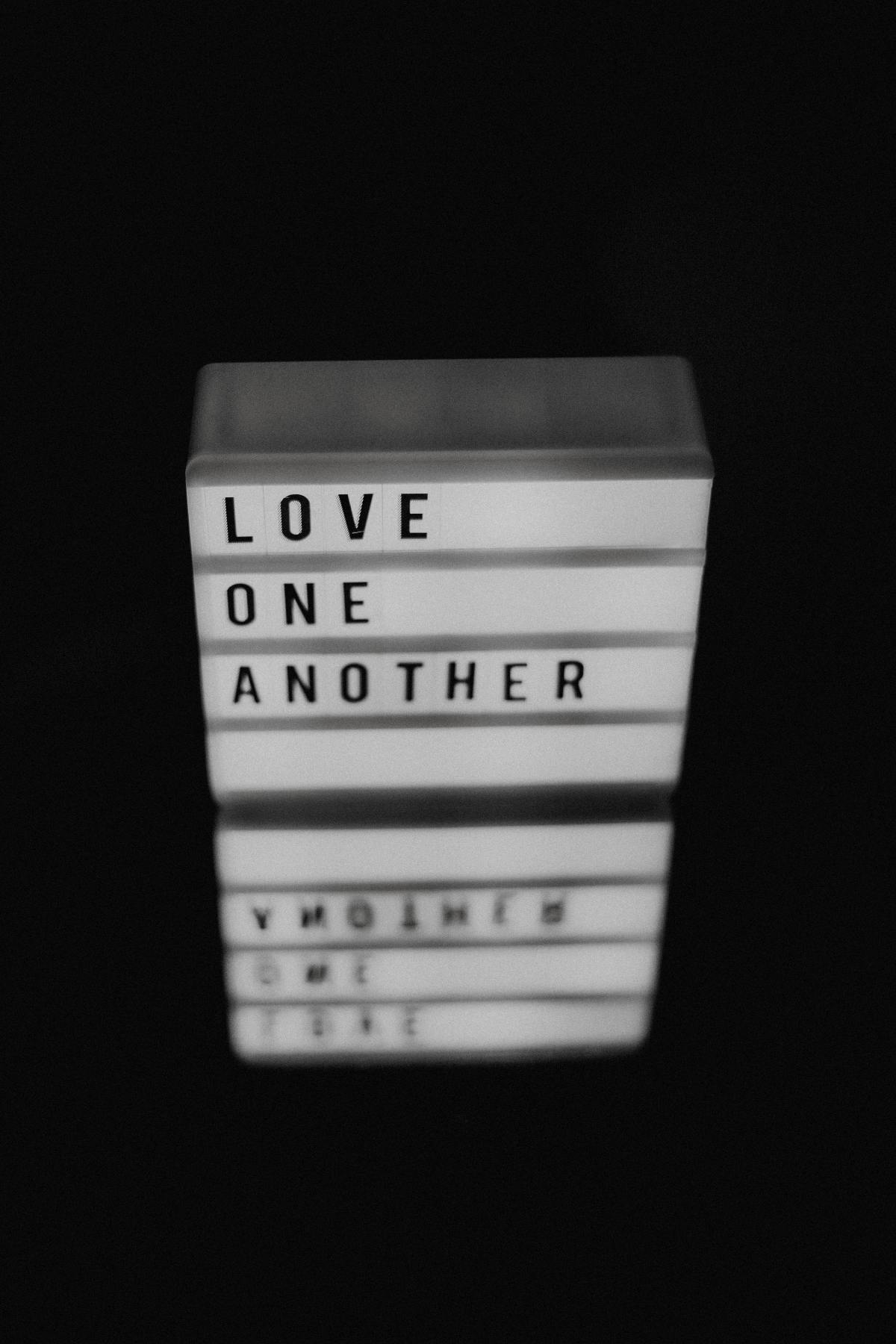 a white block against a blcack background with the words Love One Another