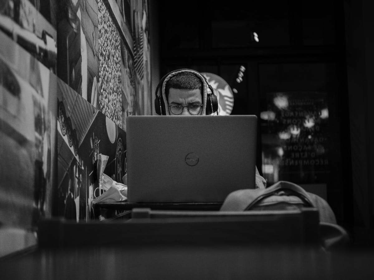 black and white image of a man in a hoodie working in his laptop