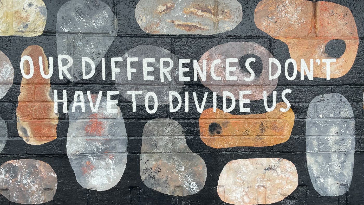 Grafiti on a wall with colorful spots and the words: Our Differences Don't Have to Divide Us.