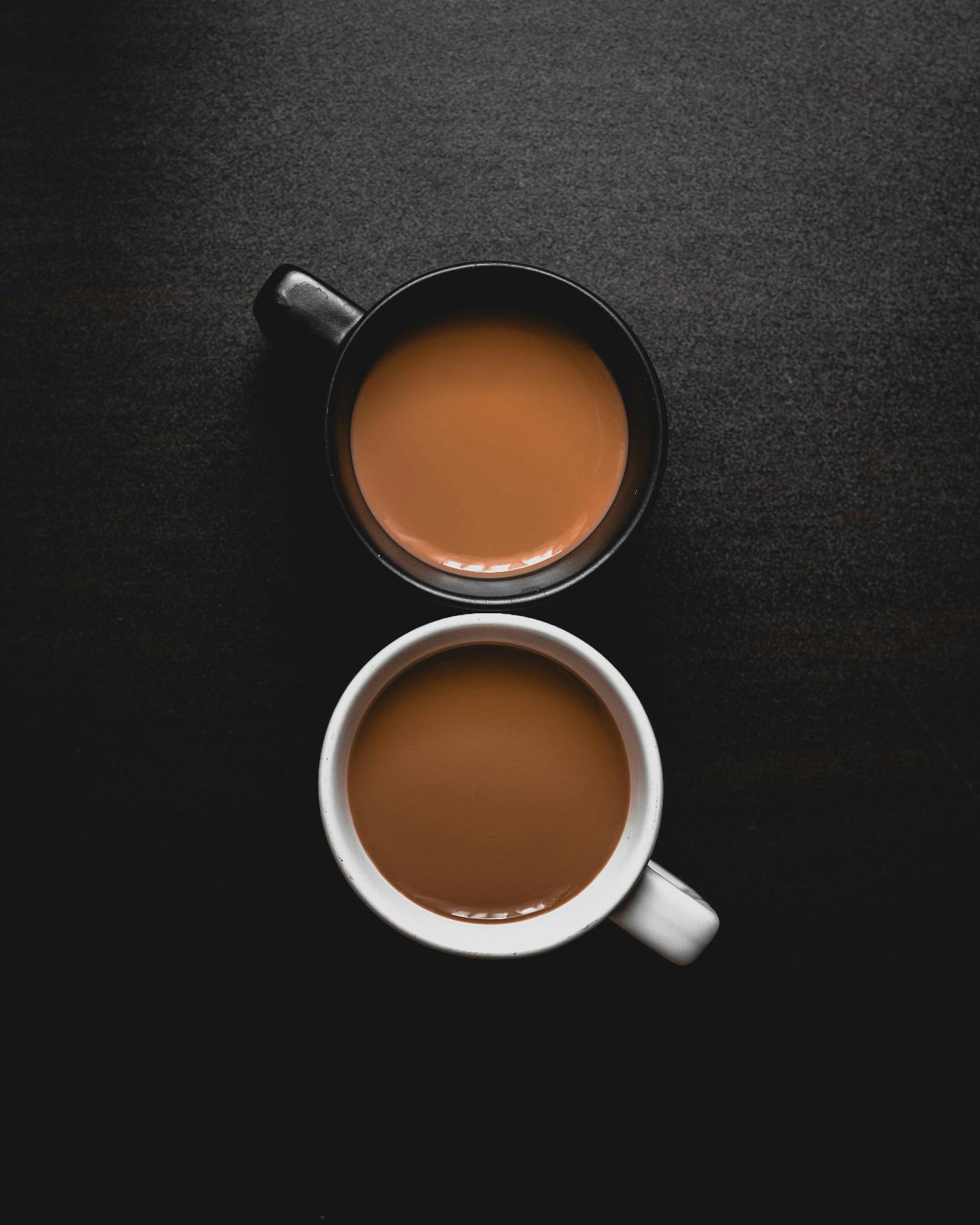 Two cups of coffee, one in a black mug, one in a white mug.