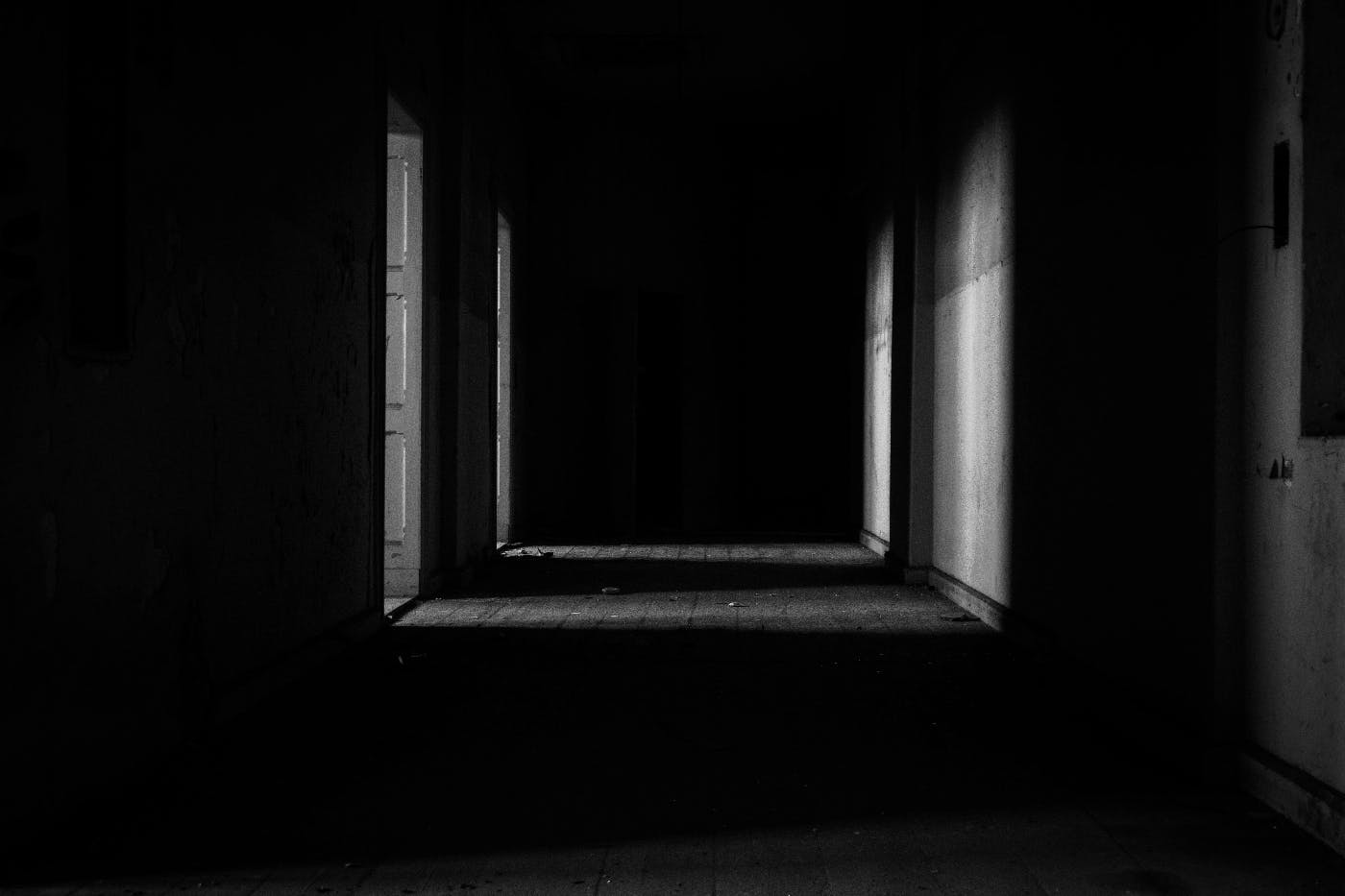 a dark hallway with light coming from open doors