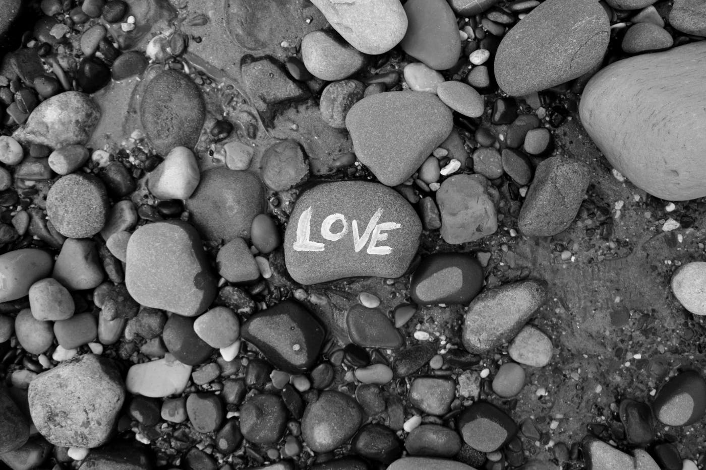 Gray scale image of stones on a beach, on a stone is painted LOVE in white