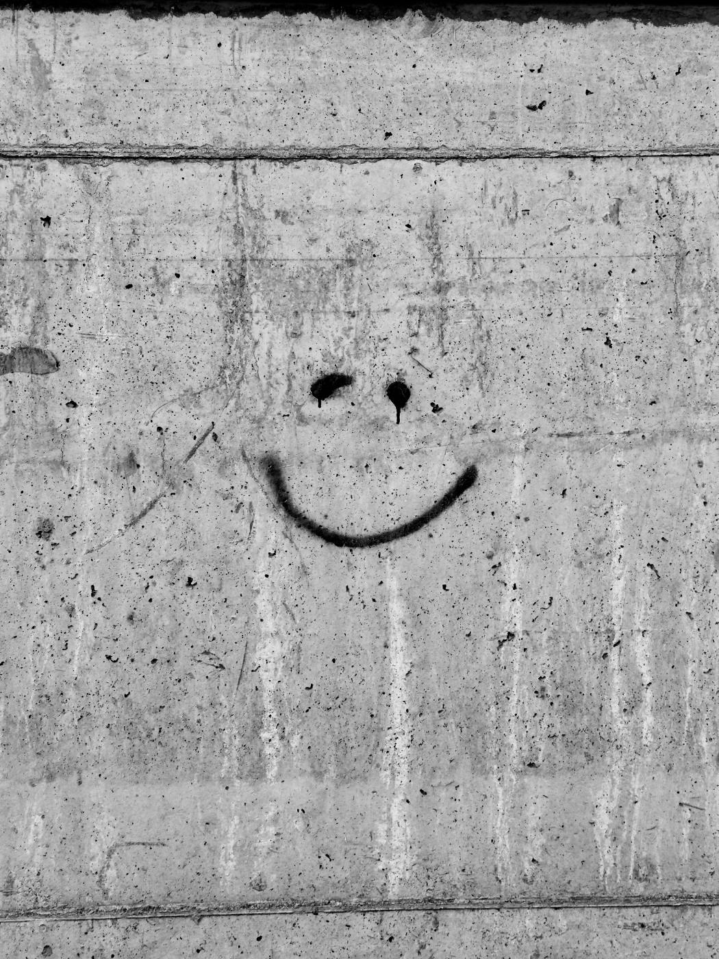 a scarred concrete wall on which someone has spray painted two dots for eyes and a smile