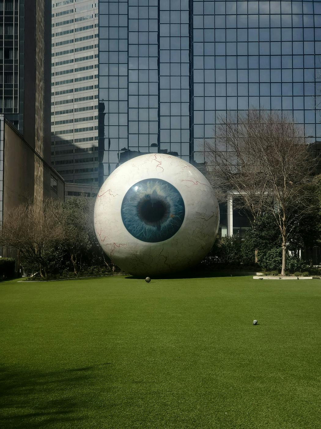 A giant eyeball on the lawn in front of a large glass building