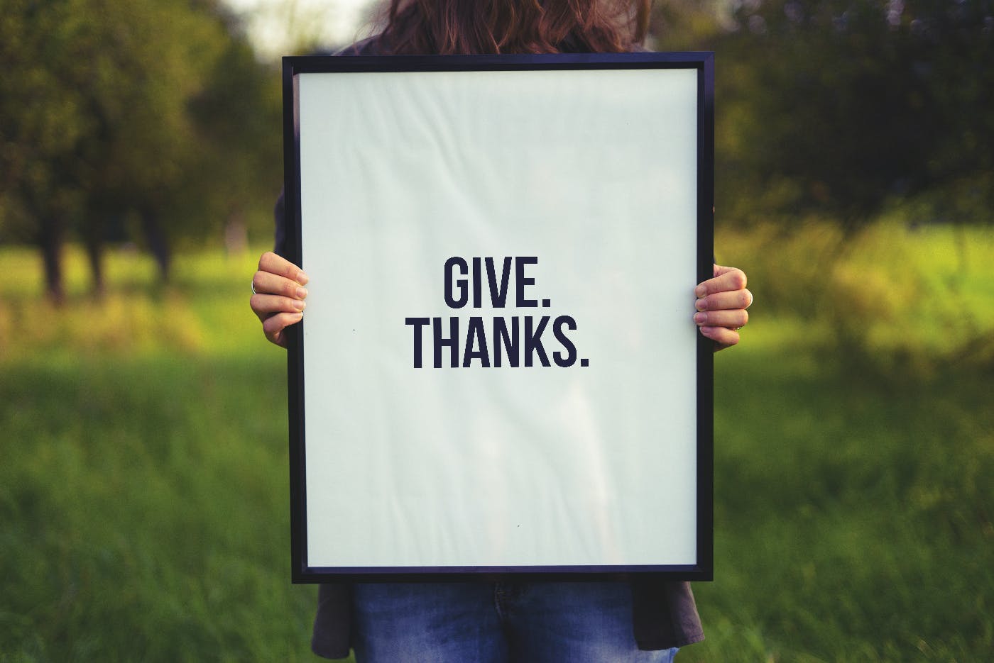 A woman holding a sign that reads: Give. Thanks.