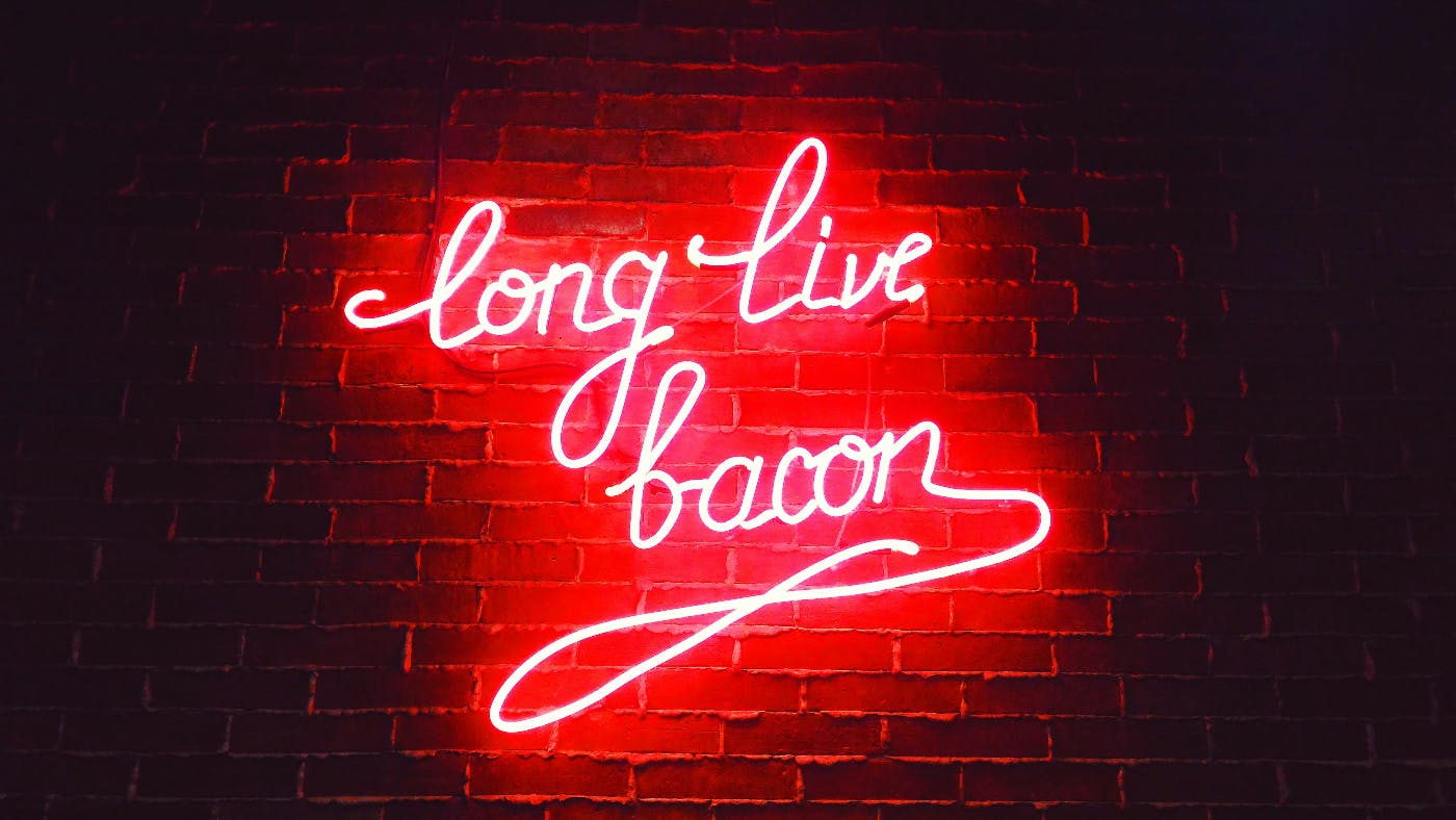 A red neon sign on a brick wall reading Long Love Bacon