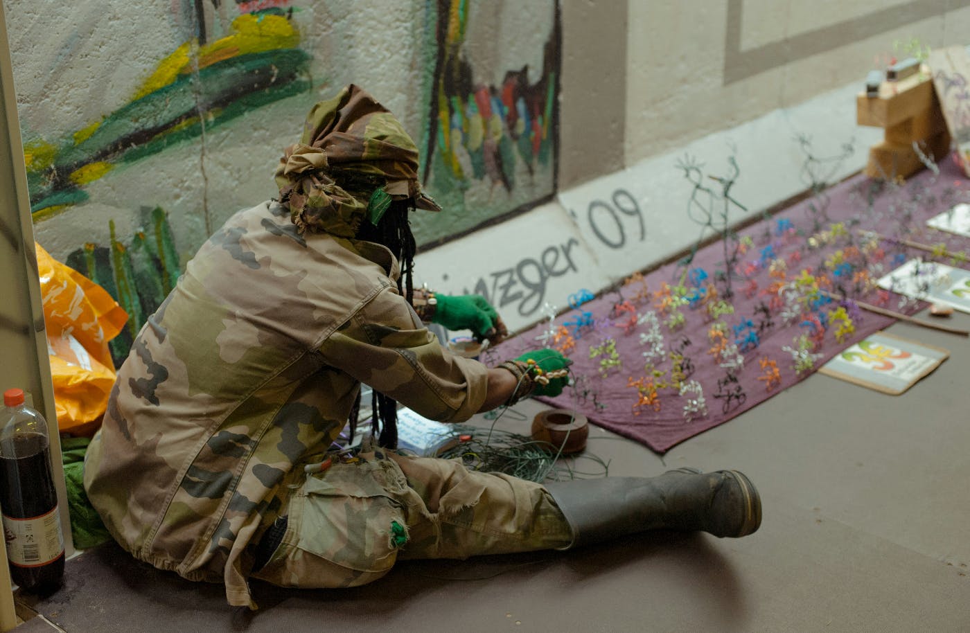 A man sitting on the sidewalk making colorful sculptures out for wire