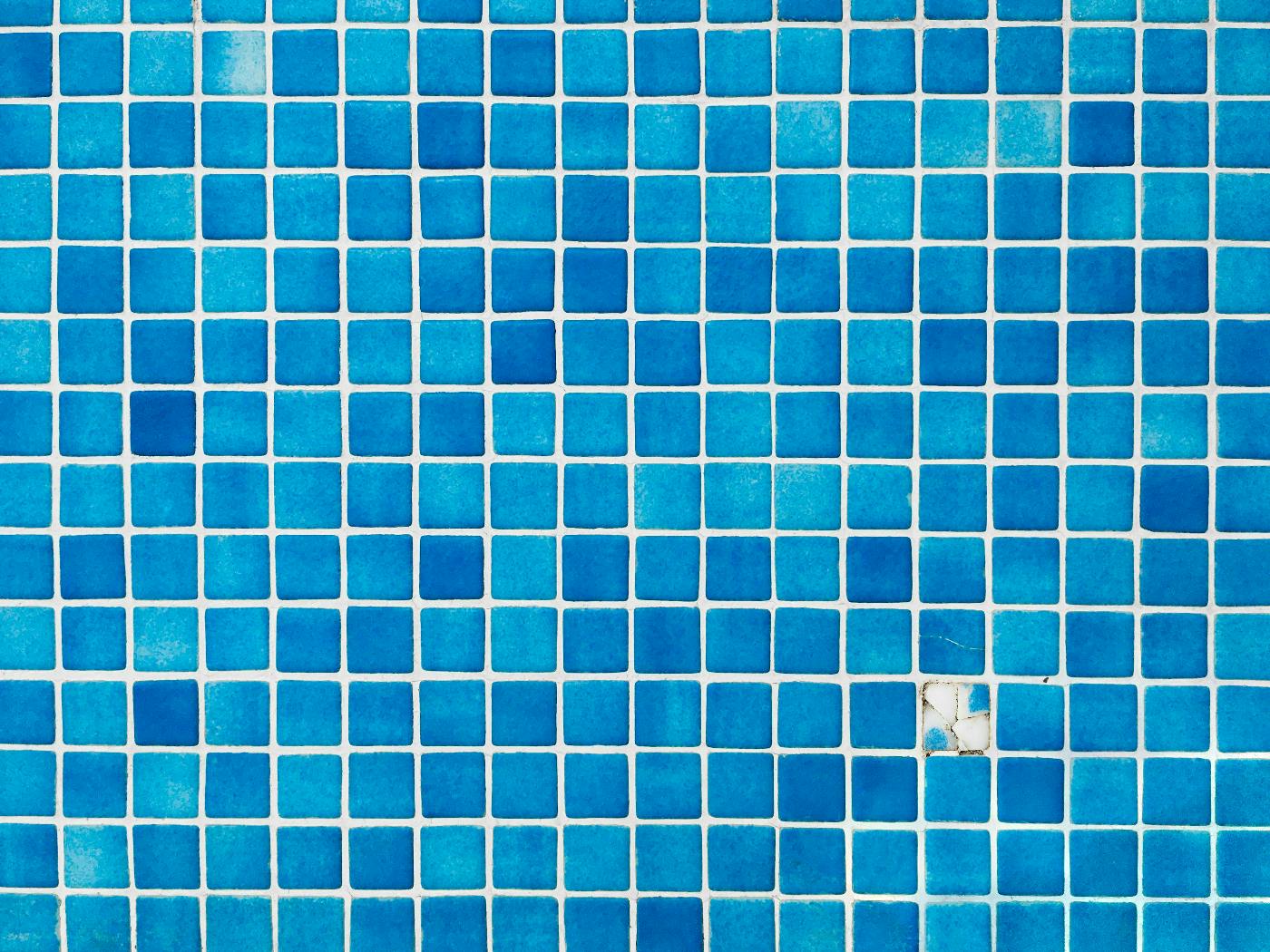 A wall of various shades of blue tile with one tile broken