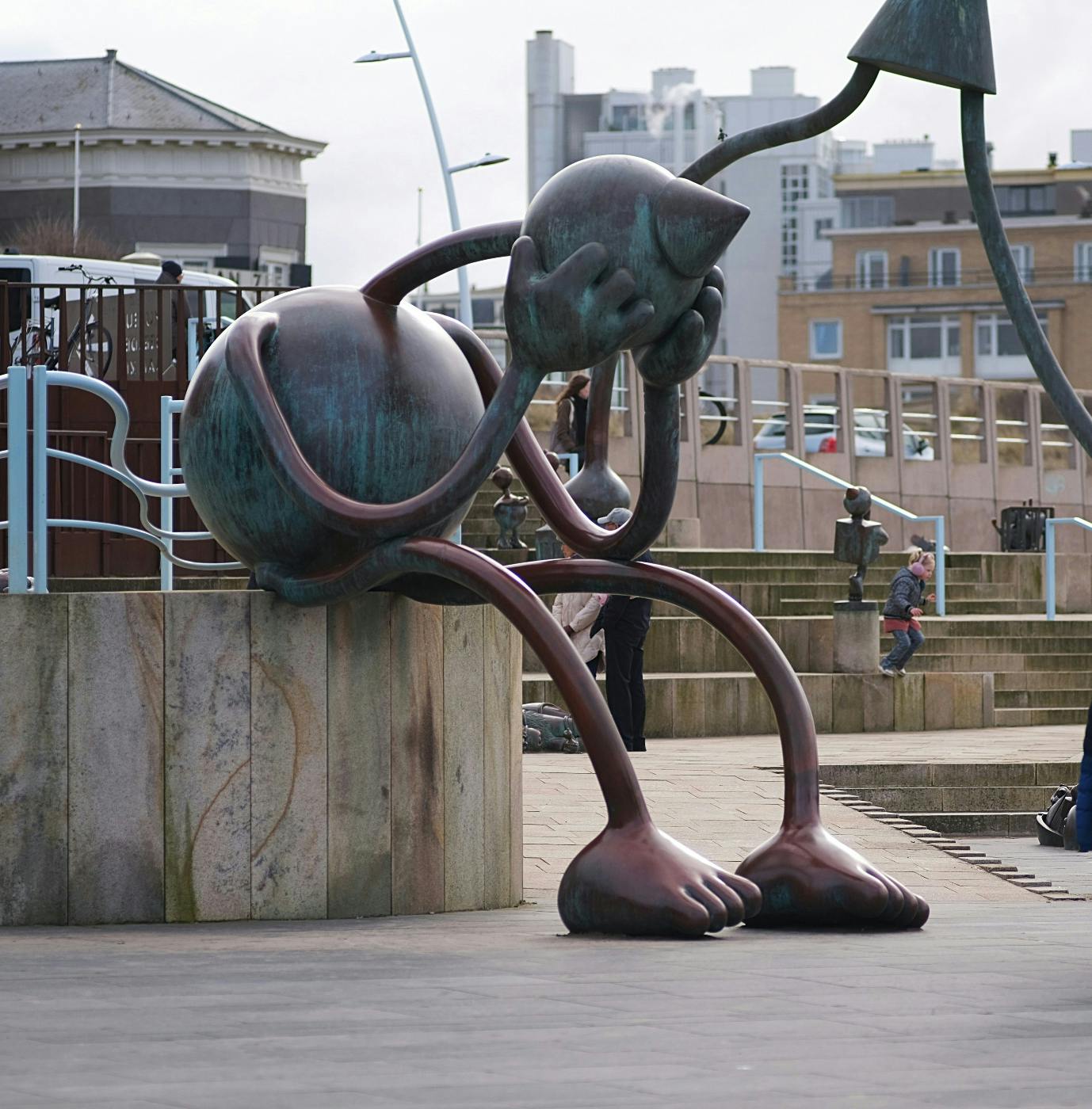 A cartoonish sculpture of a person with long noodle arms and legs with his head in his hands