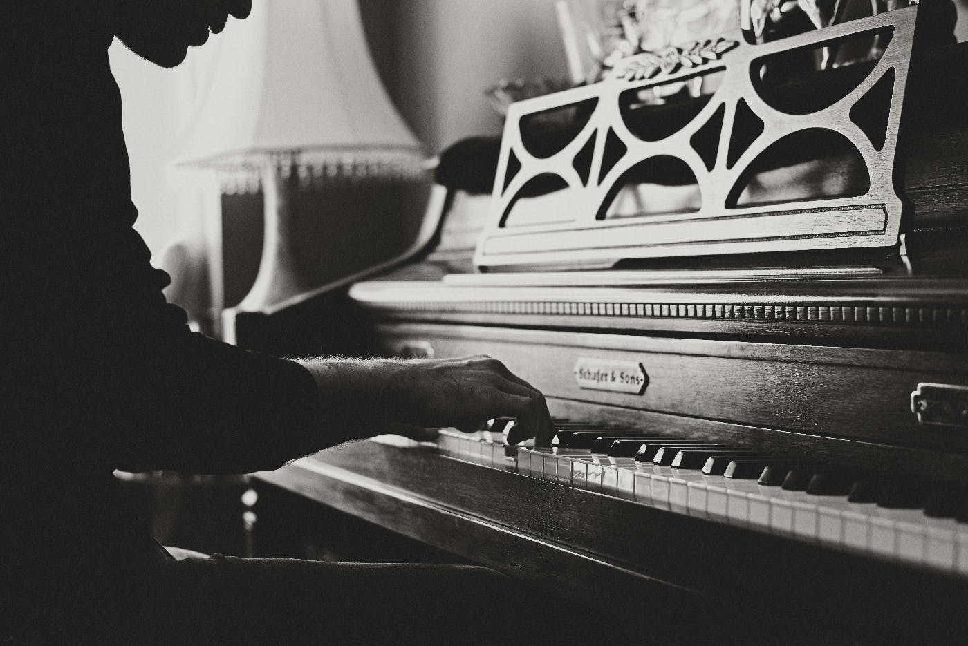 A grey scale photo of a man playing an upright piano