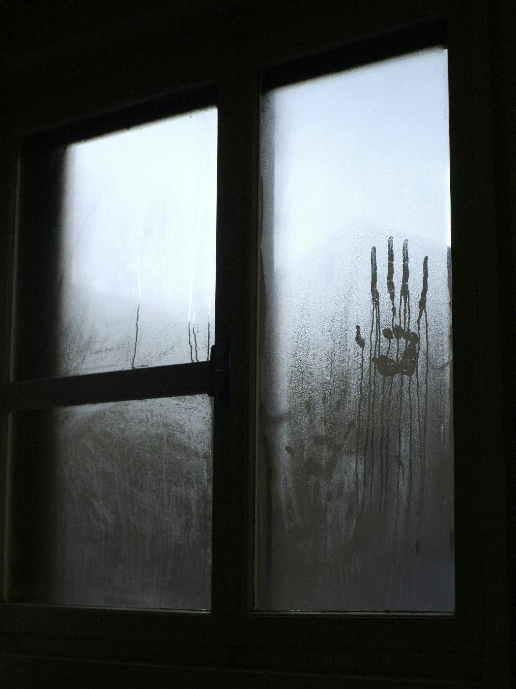 A window with a large hand print on the wet pane