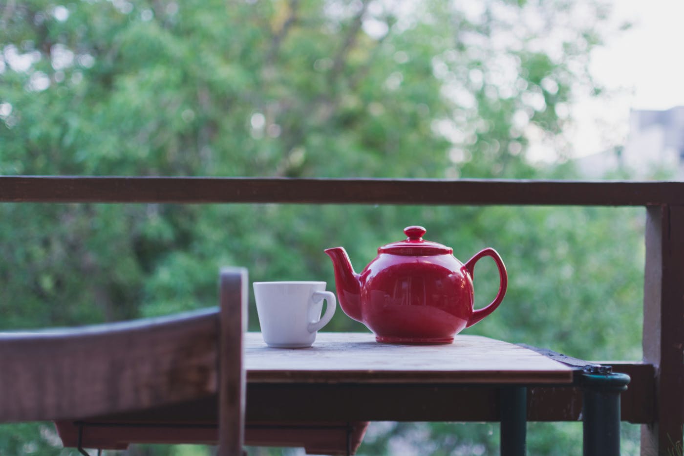 A red teapot and a white mug sitting on an outdoor table