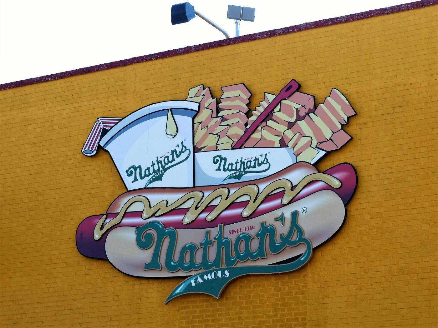 A Nathan's hot dog sign on a yellow brick wall