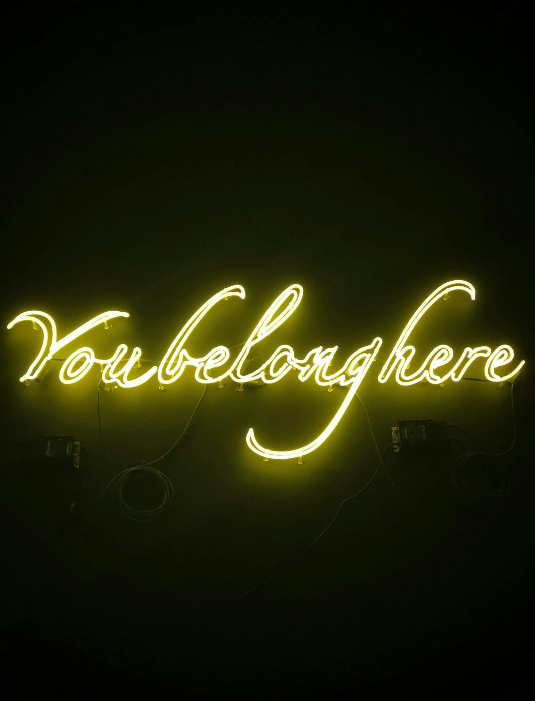 A yellow neon sign reading Your Belong Here hanging in darkness