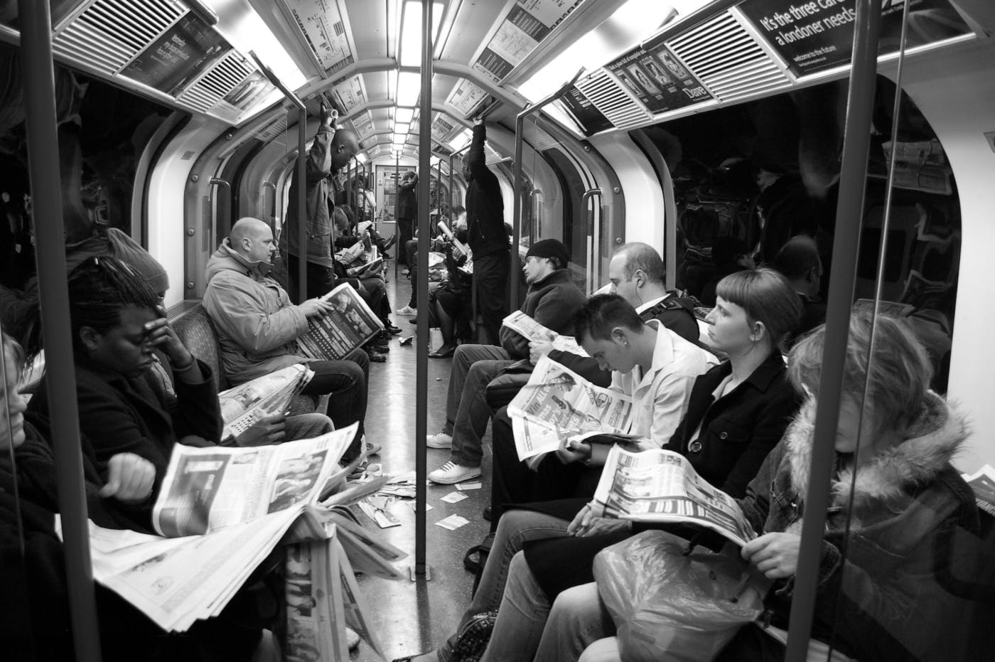 Black and white image of a subway car and everyone is reading a newspaper