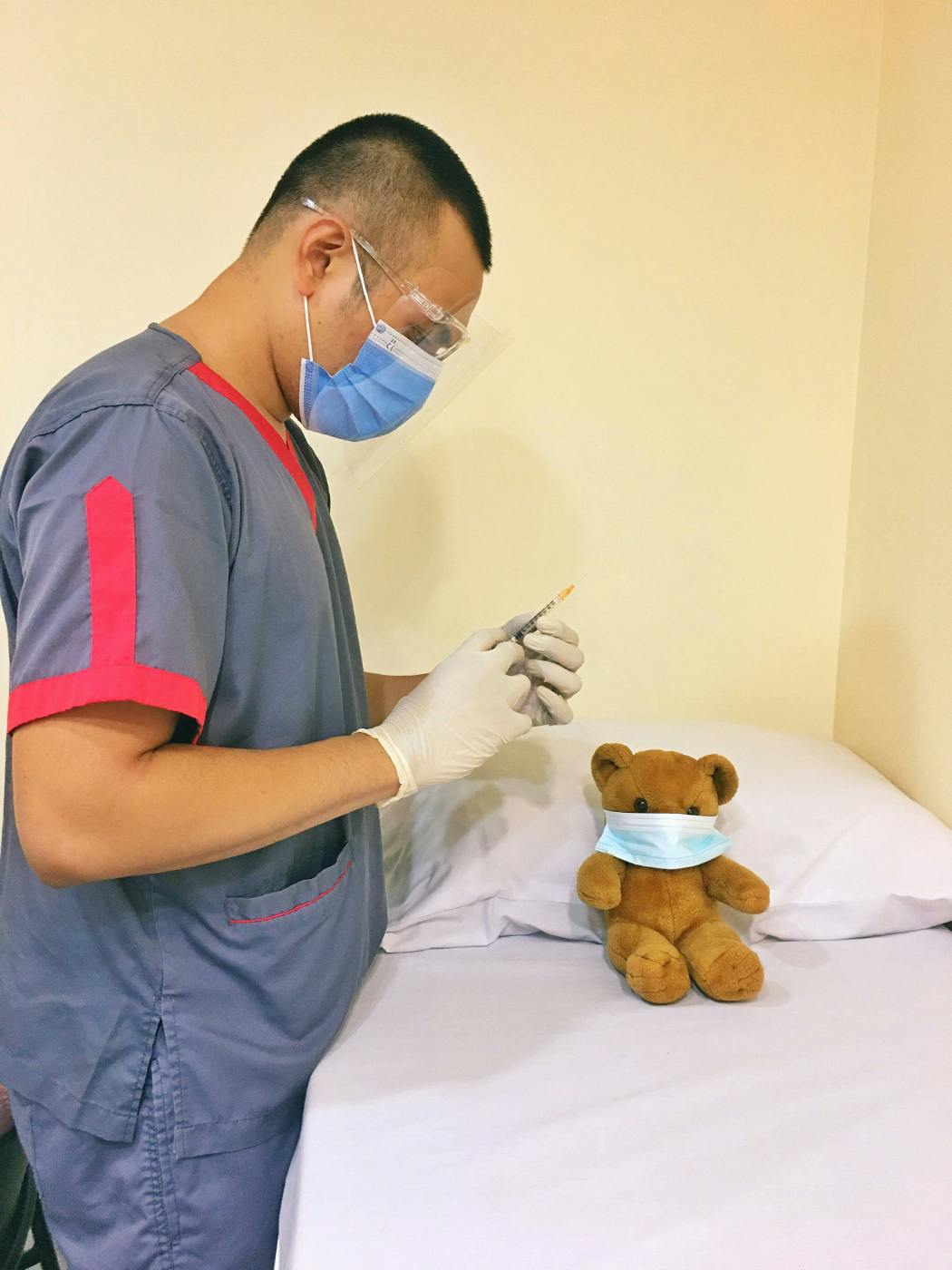 A doctor in a mask preparing to give a shot to a Teddy Bear in a mask