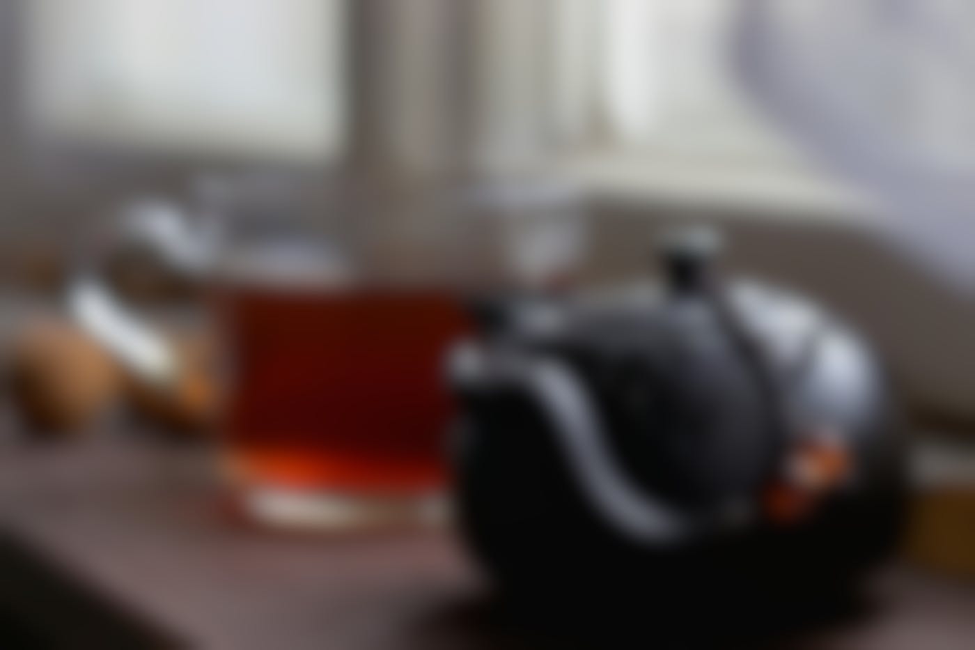 A steaming black tea pot with two amber beads and glass mug of tea