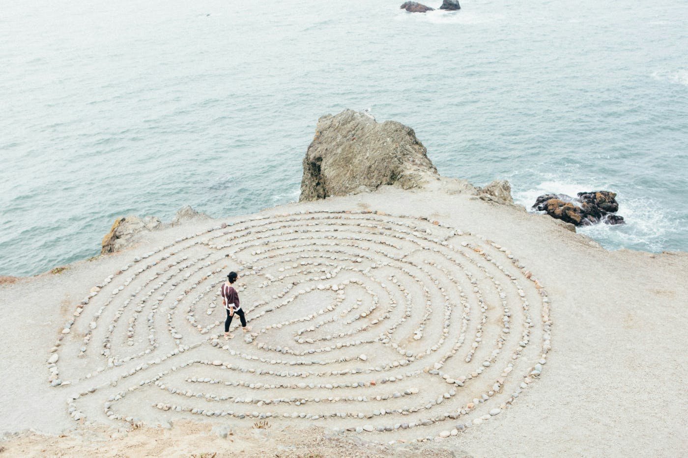 A beach and a man walking into a maze made of small stones