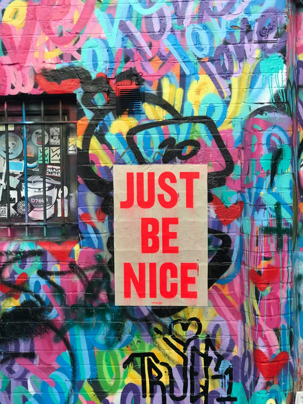 A colorfully painted wall with a sign reading Just Be Nice in red letters