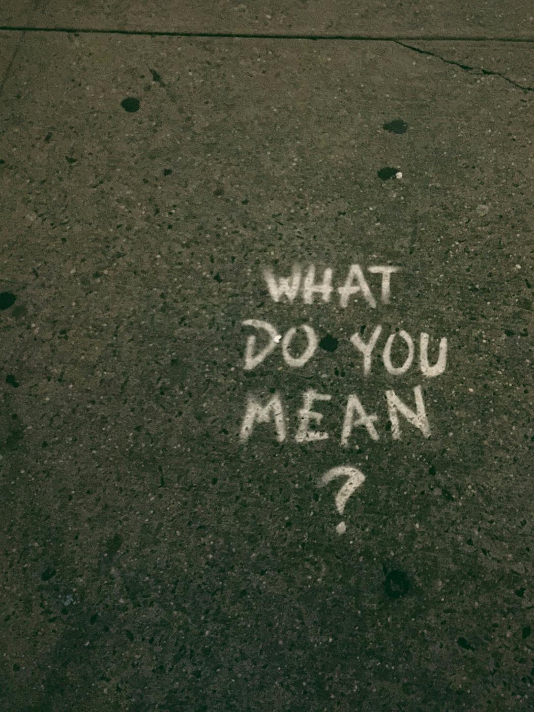 Graffiti on a sidewalk reading What Do You Mean?