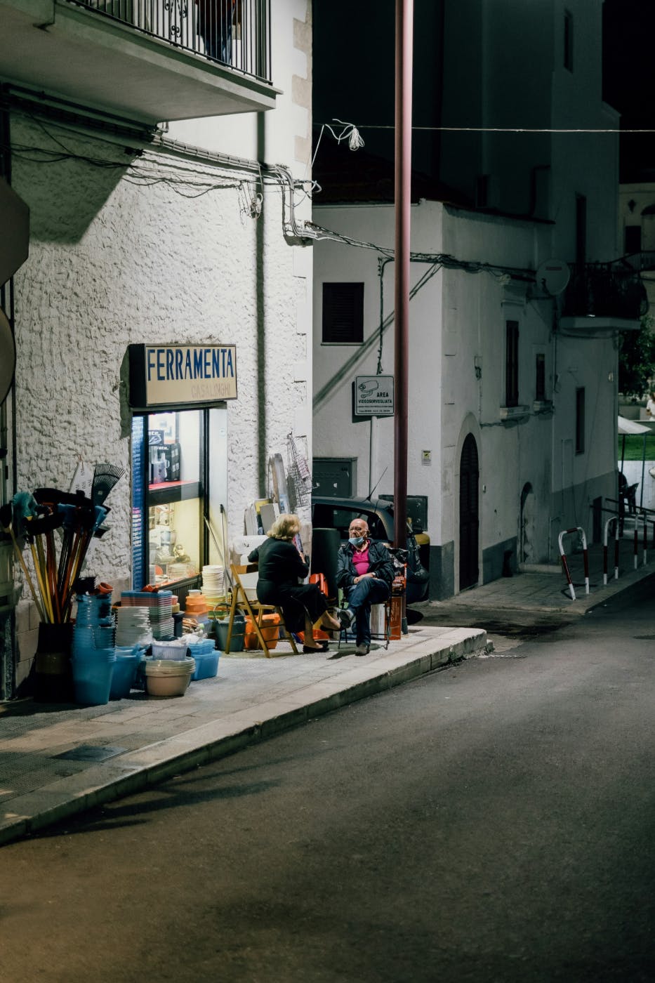 An older man and women sitting in front of an Italian hardware store chatting