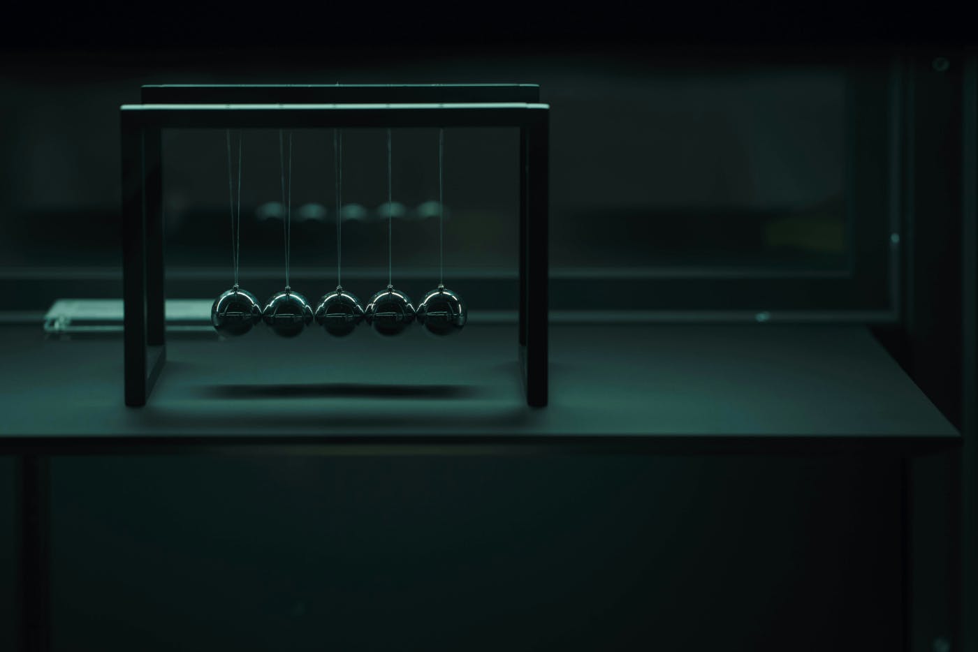 A black Newton's Cradle sitting on a green desk