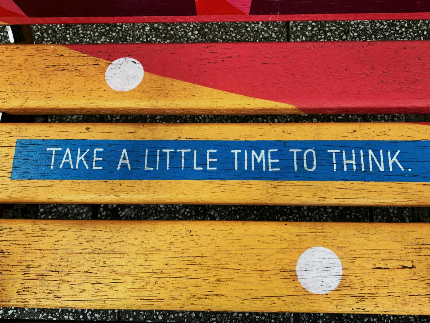 A multi colored bench with a blue strip reading Take A Little Time To Think.