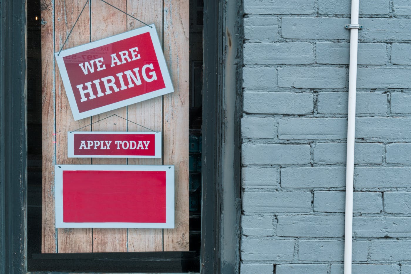 A borded up window with two red signs; We Are Hiring & Apply Today