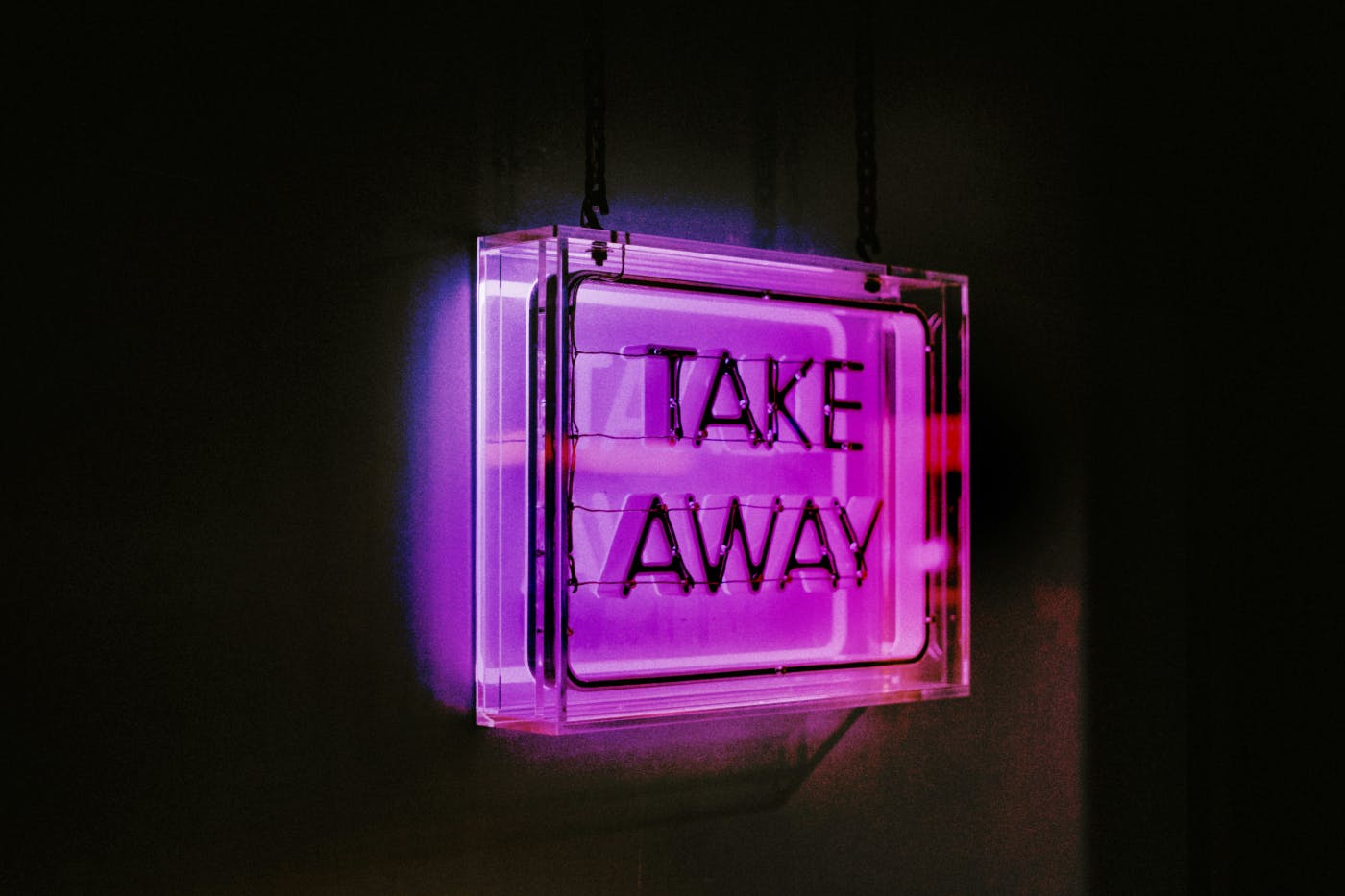 A purple neon sign in a dark room reading Take Away