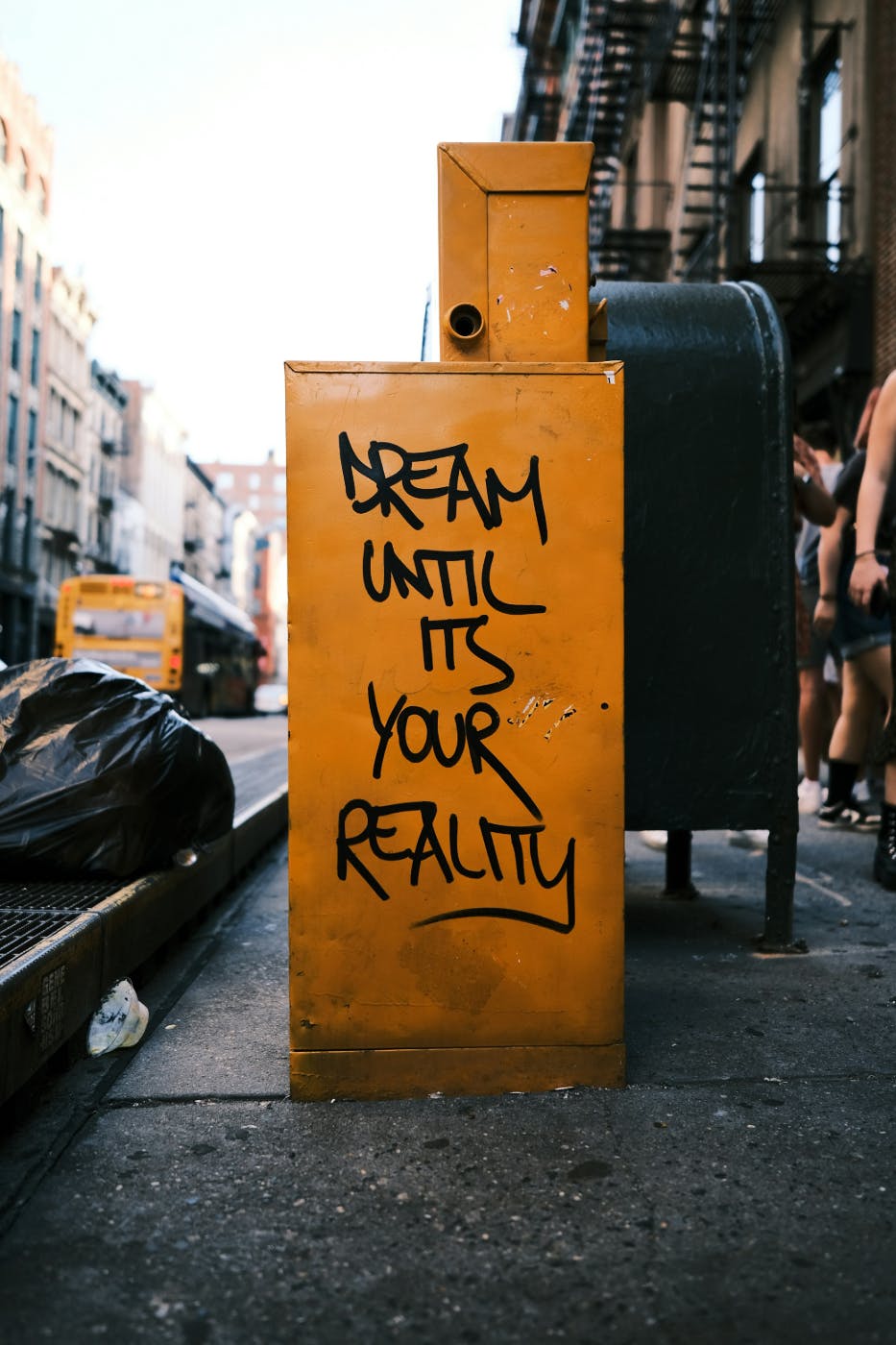 Graffiti on the side of a yellow newspaper box reading Dream Until Its Your Reality