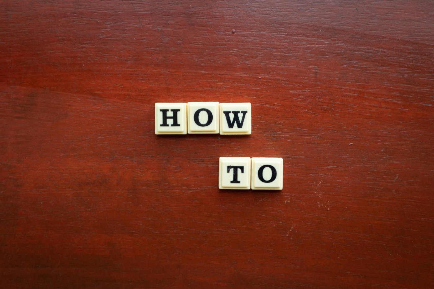 Scrabble tiles on a reddish table spelling out HOW TO