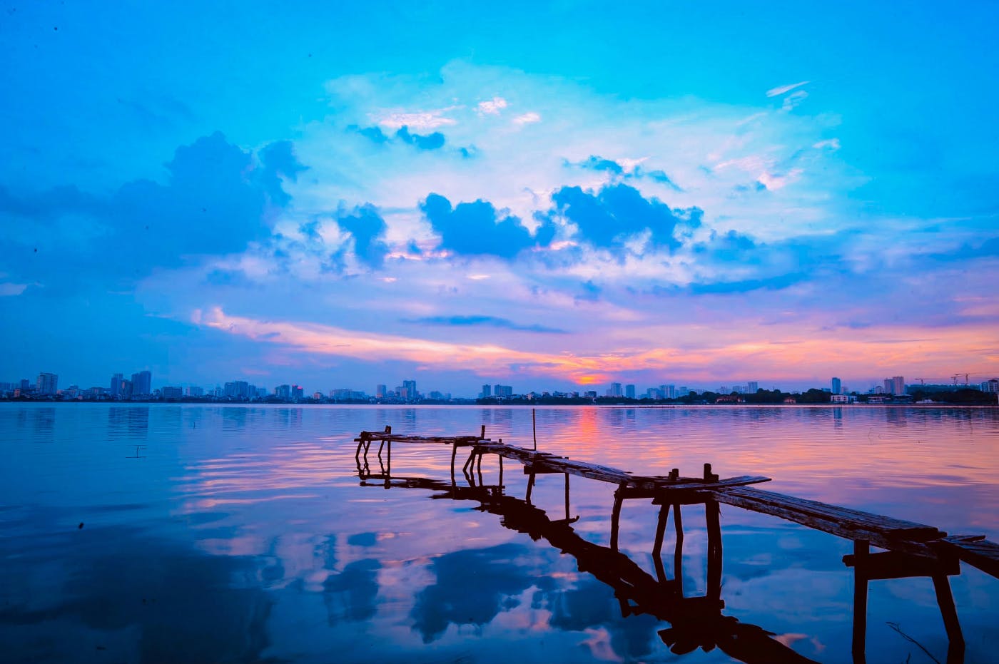 A rickety wooden doc stretching into a city's harbor at sunset
