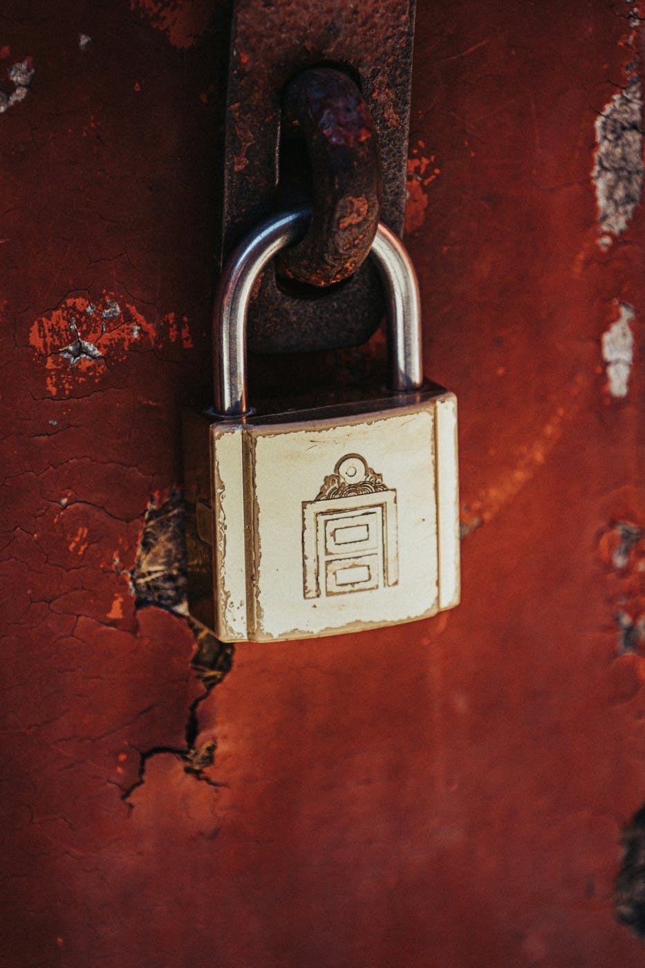 A worn, gold padlock on a rusty red door