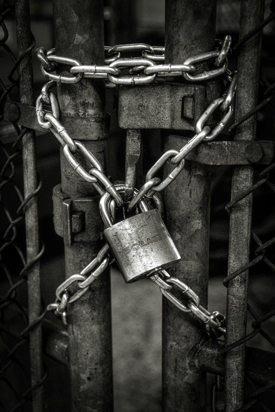 A gray scale image of a silver chain and a padlock securing a gate