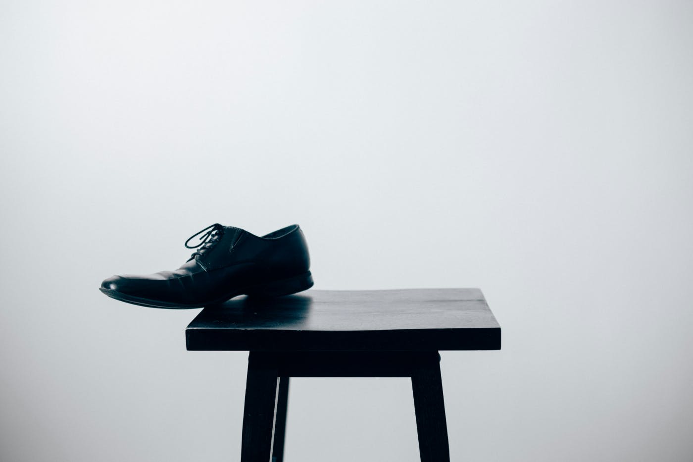 A black shoe hanging off the edge of a square black stool