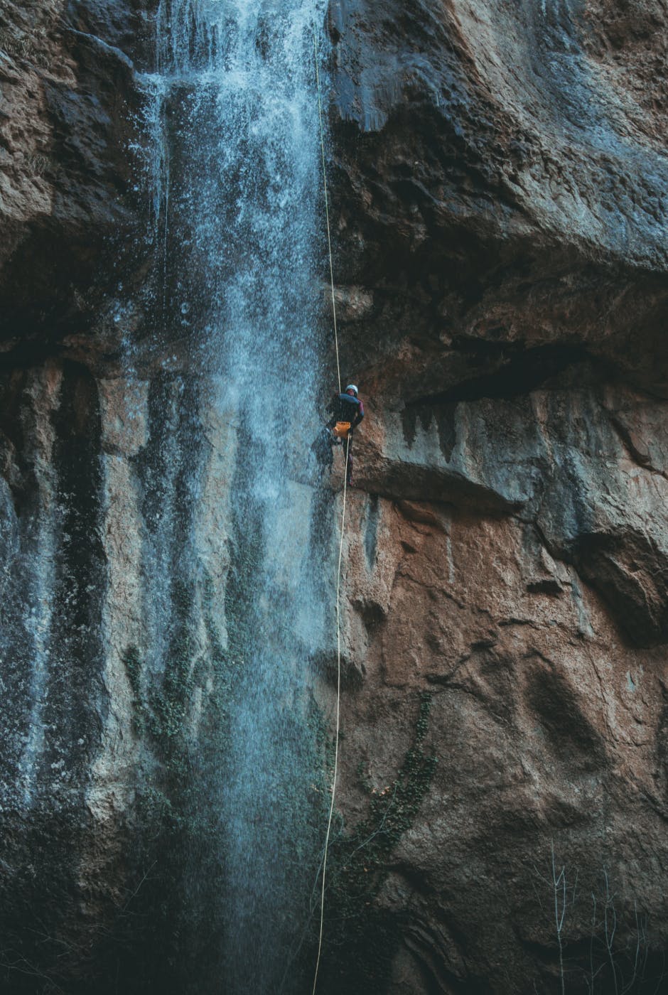 A man on a rope scaling the rock face at the edge of a waterfall