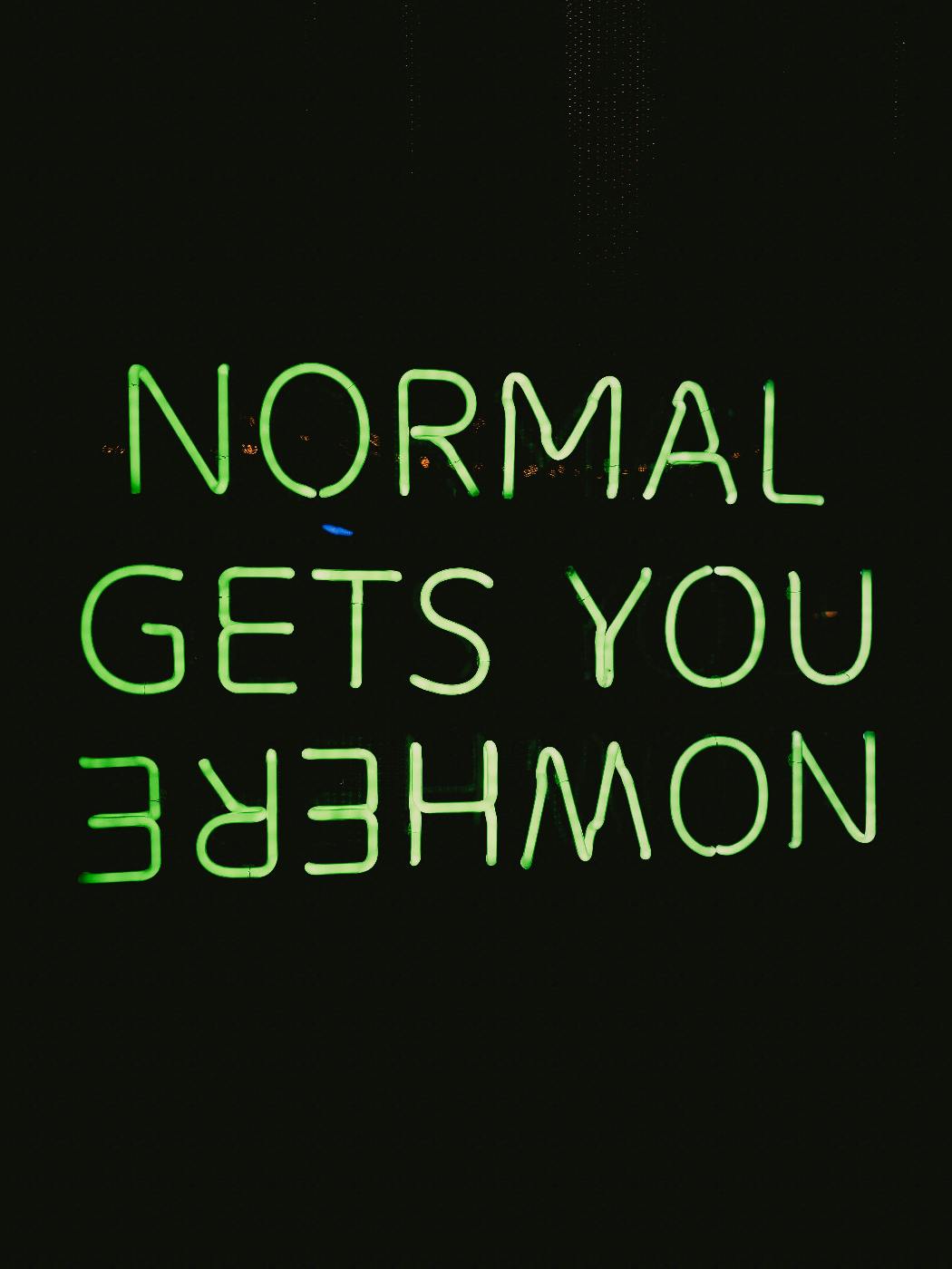 Neon sign against black reading: Normal Gets You Nowhere, with the word Nowhere upside down.
