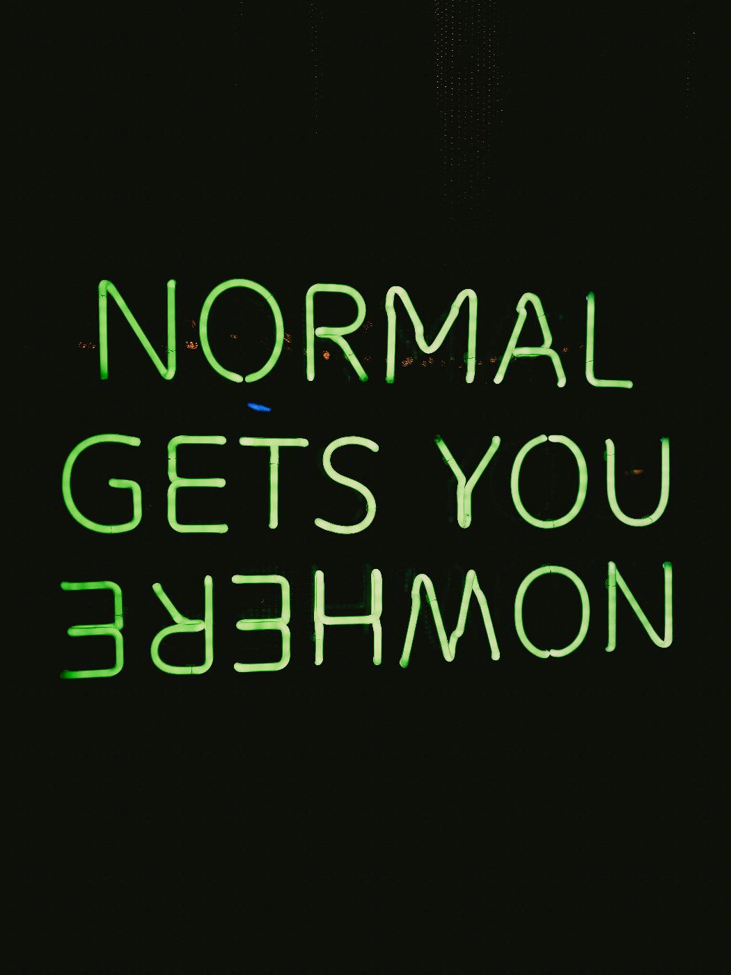 Neon sign against black reading: Normal Gets You Nowhere, with the word Nowhere upside down.