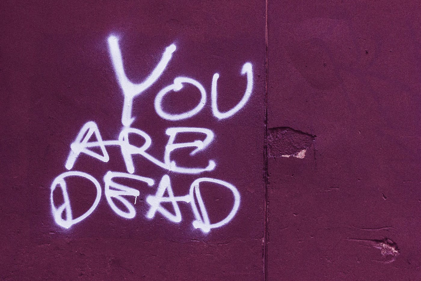 A red wall with You Are Dead spray painted on it in white
