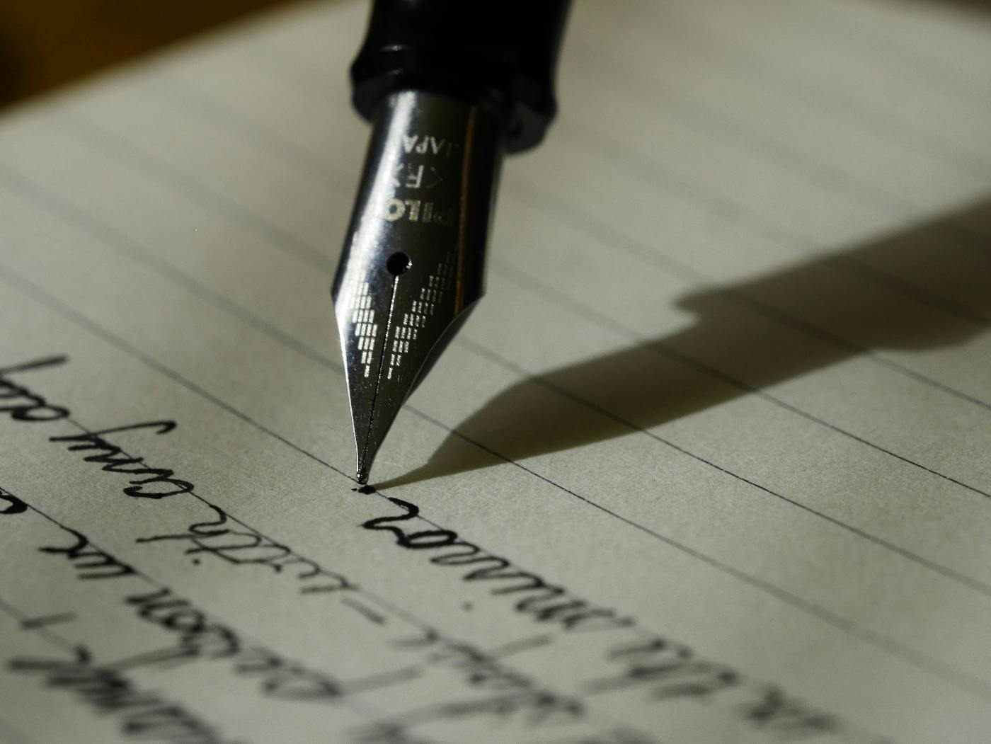 The silver tip of a fountain pen writing on a lined page