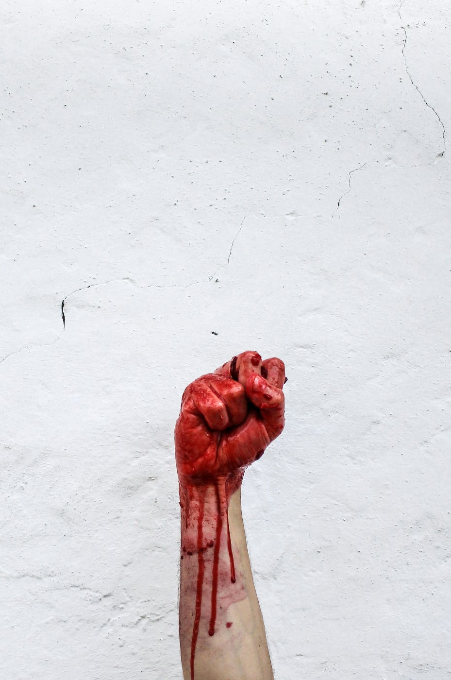 A fisted hand covered in blood raised against a white wall