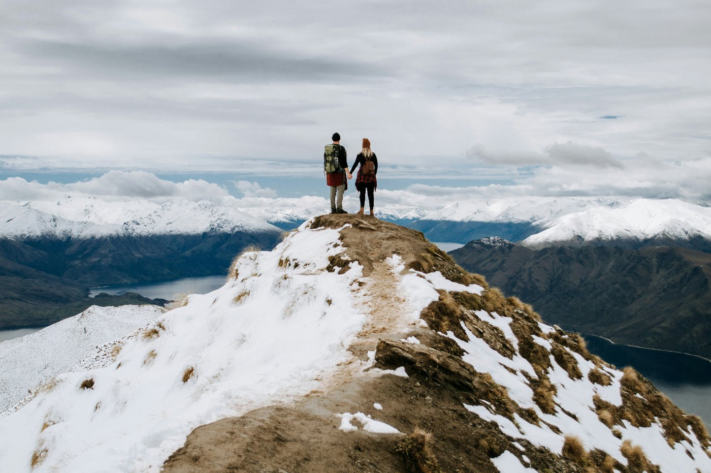 A man and woman standing at the top of mountain holding hands